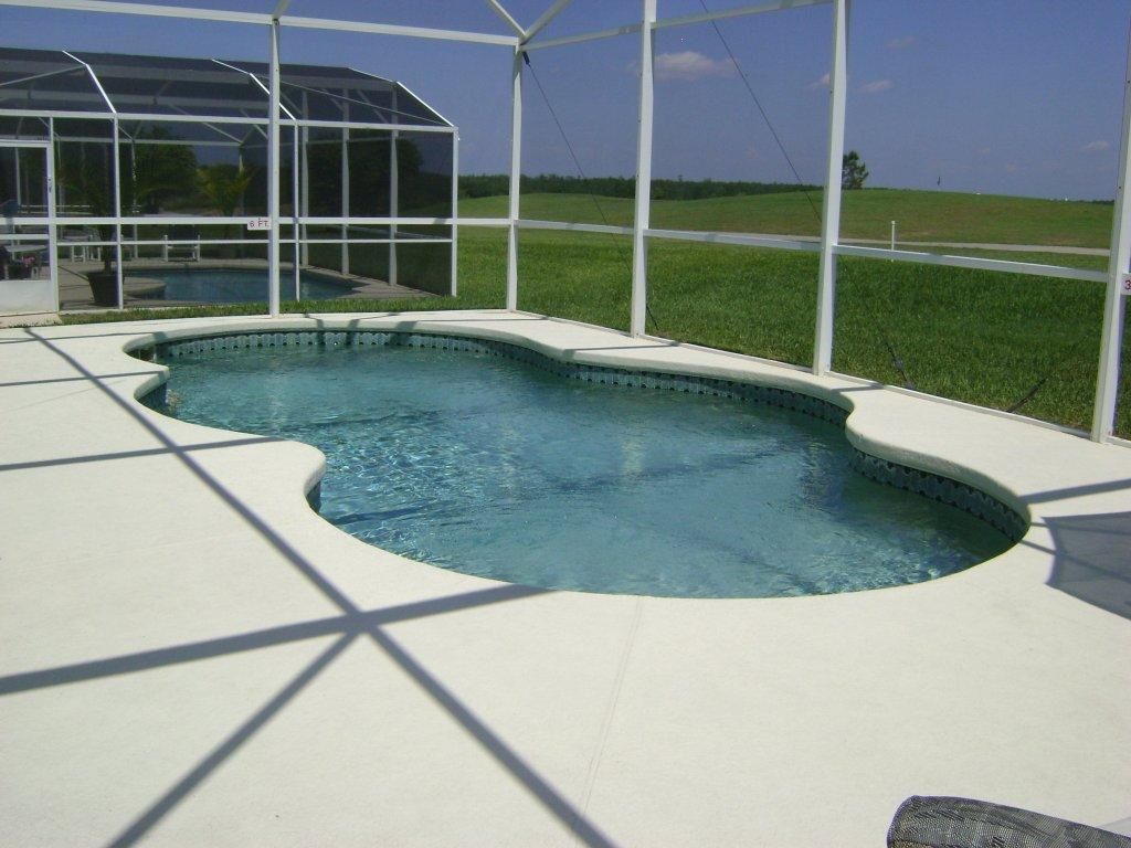 Una piscina de borde curvo, rodeada por una terraza blanca y un cerramiento de vidrio.
