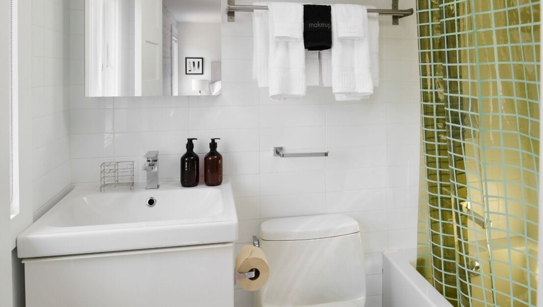 Een badkamer met een witte wasbak, toilet en bad. Op de wasbak staan twee flesjes shampoo en conditioner.