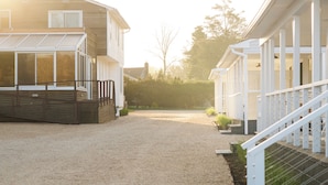 A residential property with a covered patio, a gravel driveway, and a fenced yard. - The Penny Lane (Hampton Bays)
