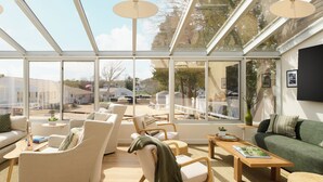 A sunlit room with a glass ceiling, a sofa, chairs, a table, and a view of the outside. - The Penny Lane (Hampton Bays)