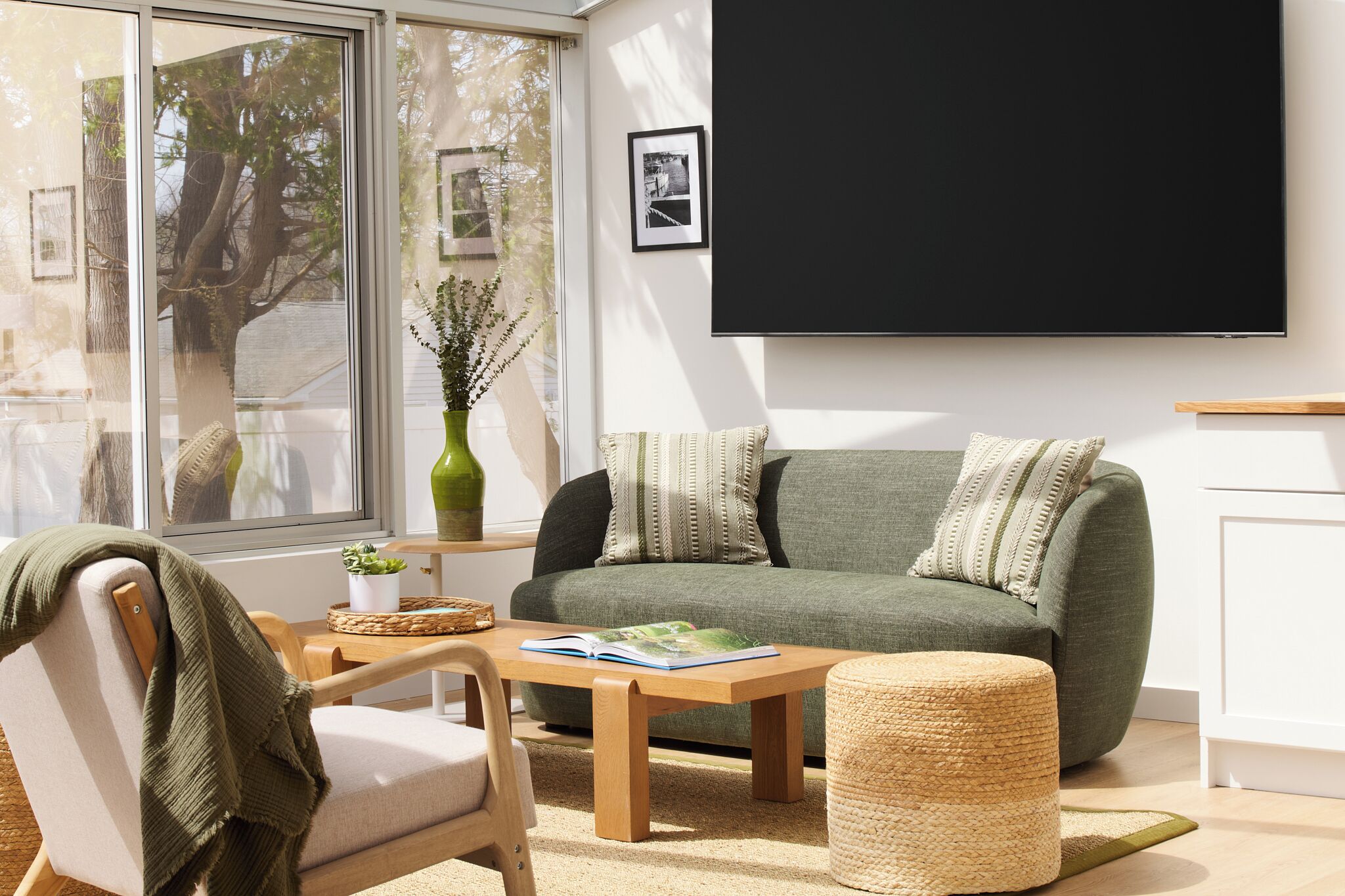 Un salon moderne comprenant un canapé, une table basse, un fauteuil, une grande fenêtre et un téléviseur fixé au mur.