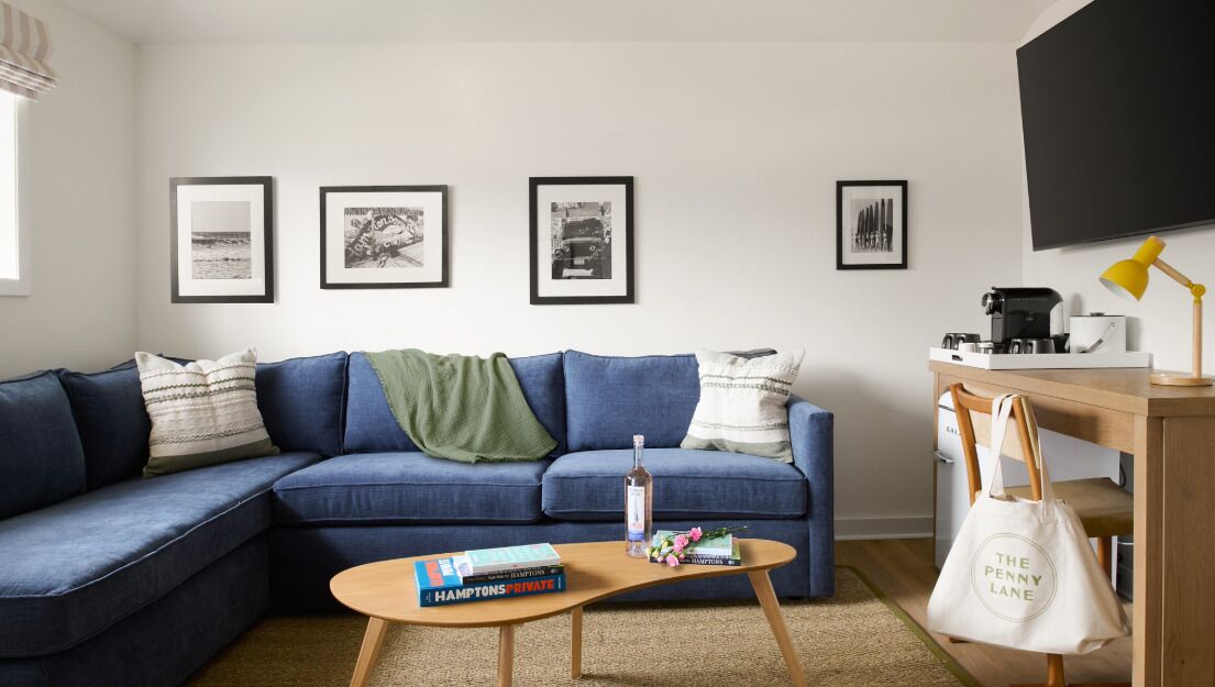 A living room with a blue sofa, a coffee table with books, a lamp, and a TV on the wall.