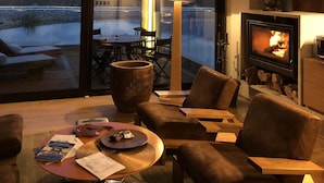 A cozy living room with a large window overlooking a body of water and mountains, a fireplace, and comfortable seating. - Casa de Uco Vineyards & Wine Hotel (Tunuyan)