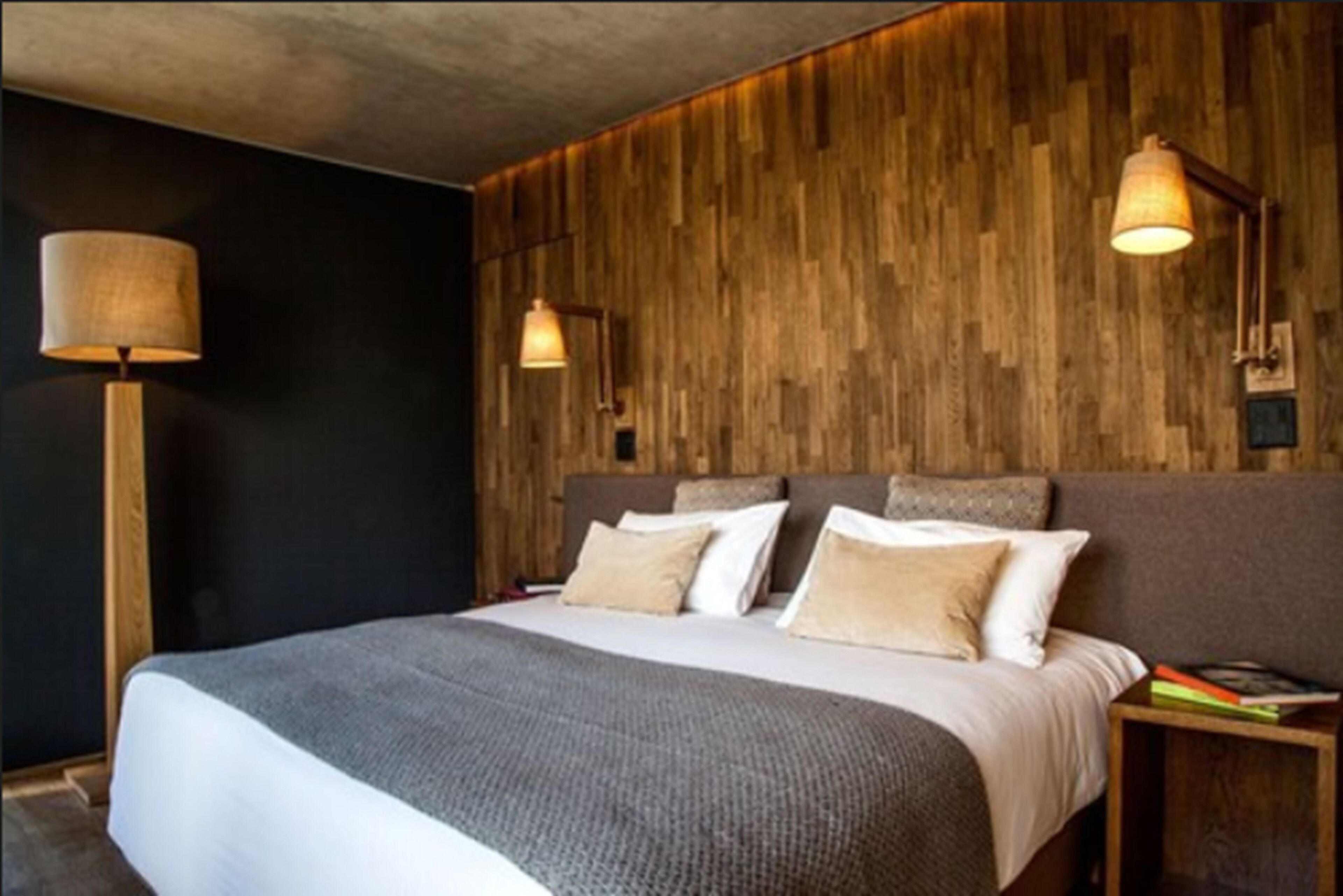 A modern bedroom with a large bed, wooden panel wall, and two bedside lamps.