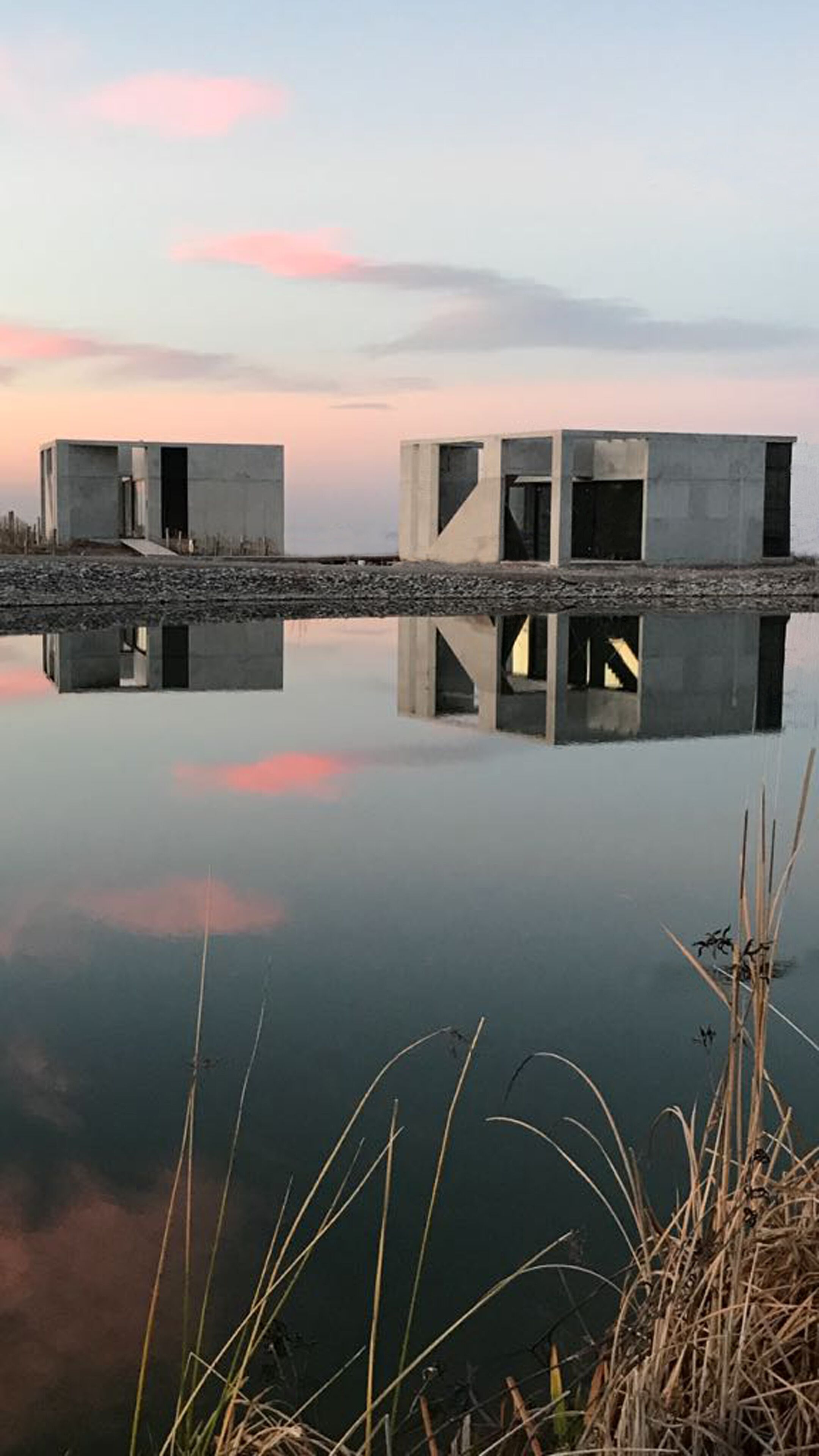 A modern concrete structure over a body of water, reflecting the sky and surroundings.