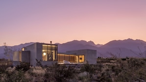 A modern, minimalist house with large glass windows, a flat roof, and a desert landscape in the background. - Casa de Uco Vineyards & Wine Hotel (Tunuyan)