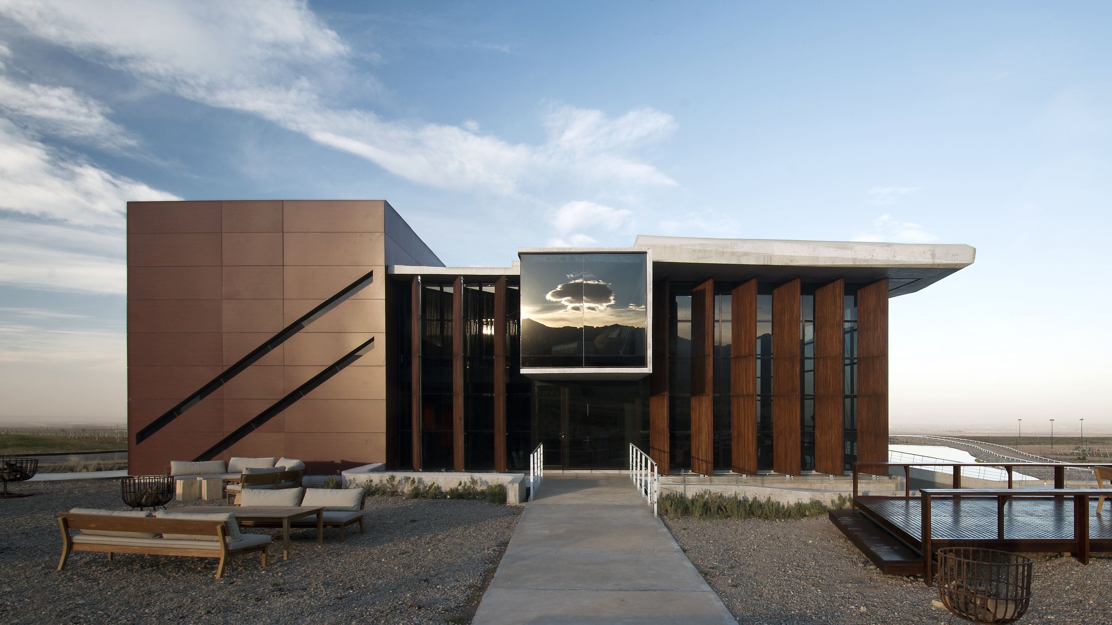 A modern building with a large glass facade, outdoor seating, and a view of the landscape.