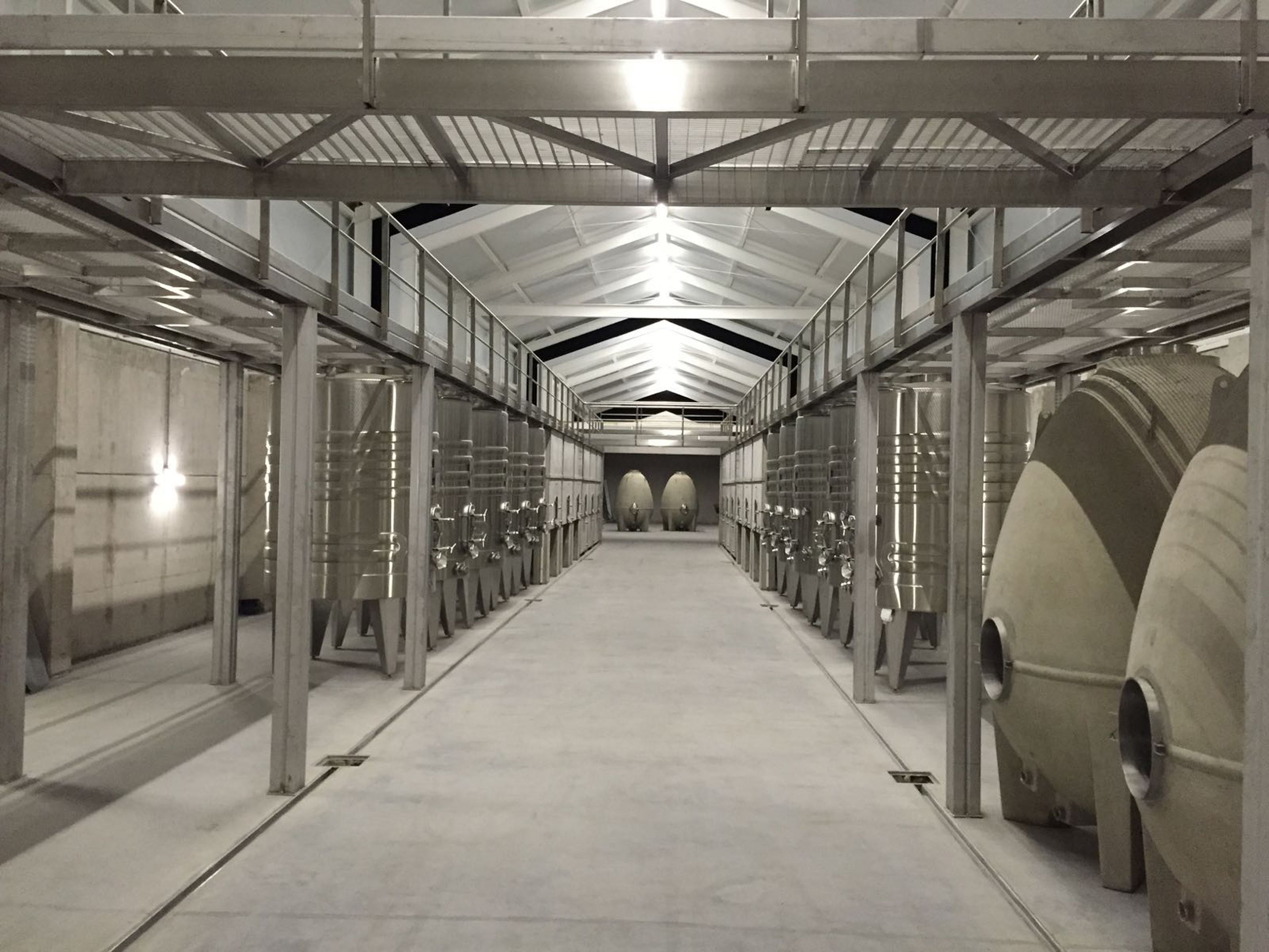 Un largo y estrecho pasillo con hileras de tanques cilíndricos a ambos lados, sostenidos por vigas y columnas de metal, bajo un techo metálico.