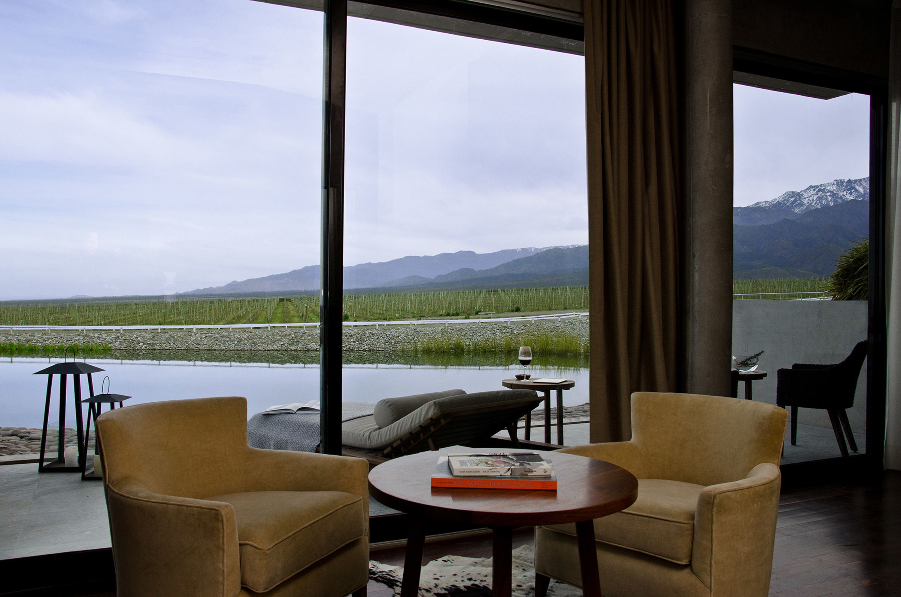 A room with a large window overlooking a lake and mountains, furnished with two armchairs and a small table.