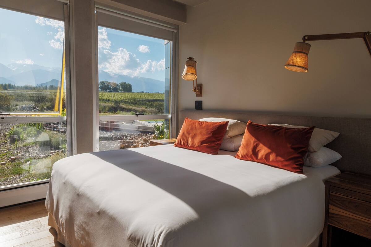 A bedroom with a large bed, two bedside lamps, and a view of a landscape through a large window.