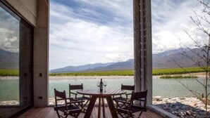 A wooden deck with a table and chairs overlooking a river and mountains. - Casa de Uco Vineyards & Wine Hotel (Tunuyan)