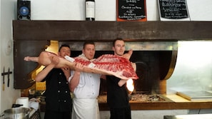 A restaurant interior with a large fire grill, a chalkboard menu, and a wine bottle on the wall. - Friendly Auberge - Hostel (Colomiers)