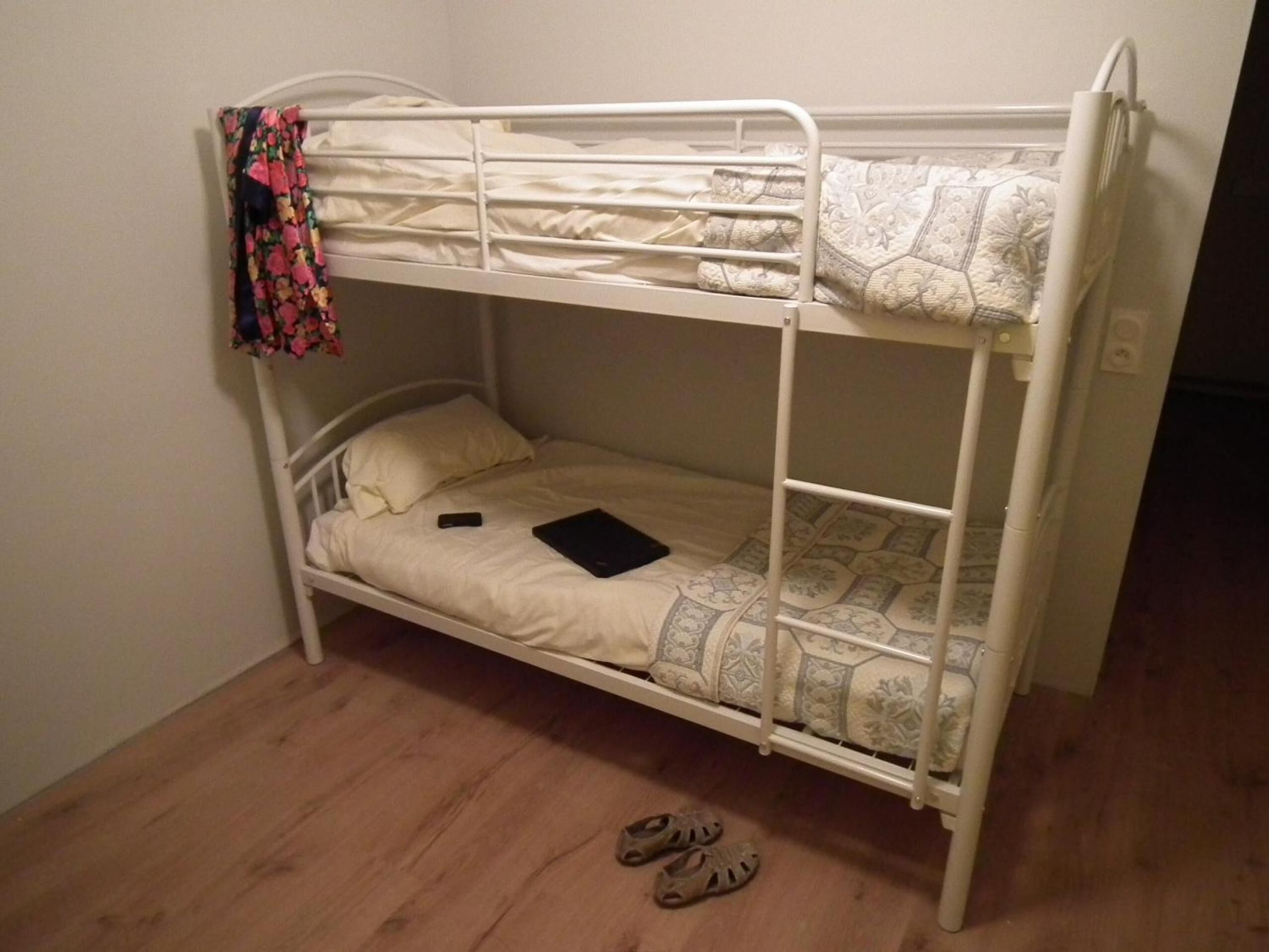 A bunk bed with a mattress, pillows, a book, and a pair of sandals on the floor.
