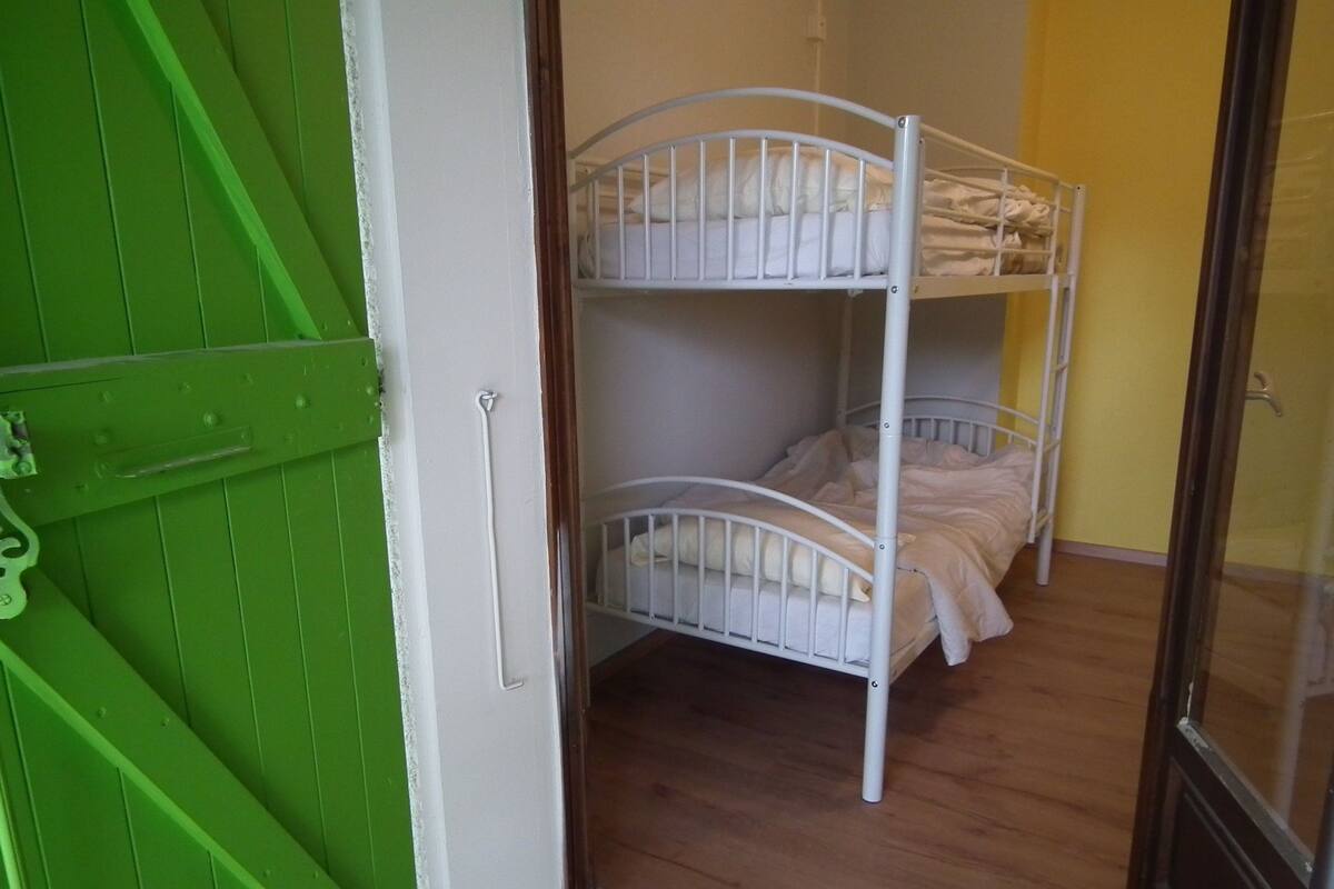 A bunk bed room with a green door and wooden flooring.