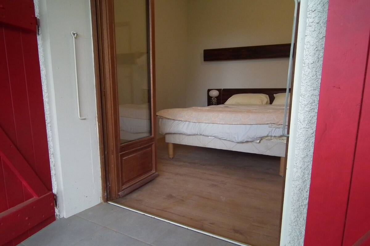 A bedroom with a bed, a wooden floor, and a red door.