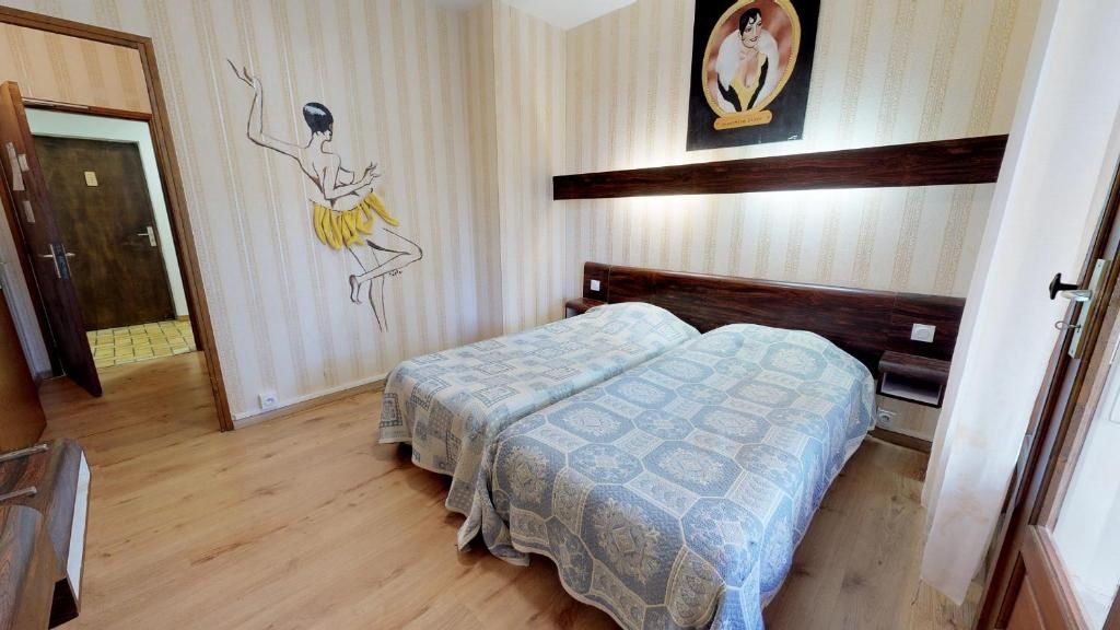 Ein Hotelzimmer mit zwei Betten, Holzboden, Wand mit Wandgemälde einer Ballerina und einem gerahmten Bild über dem Bett.