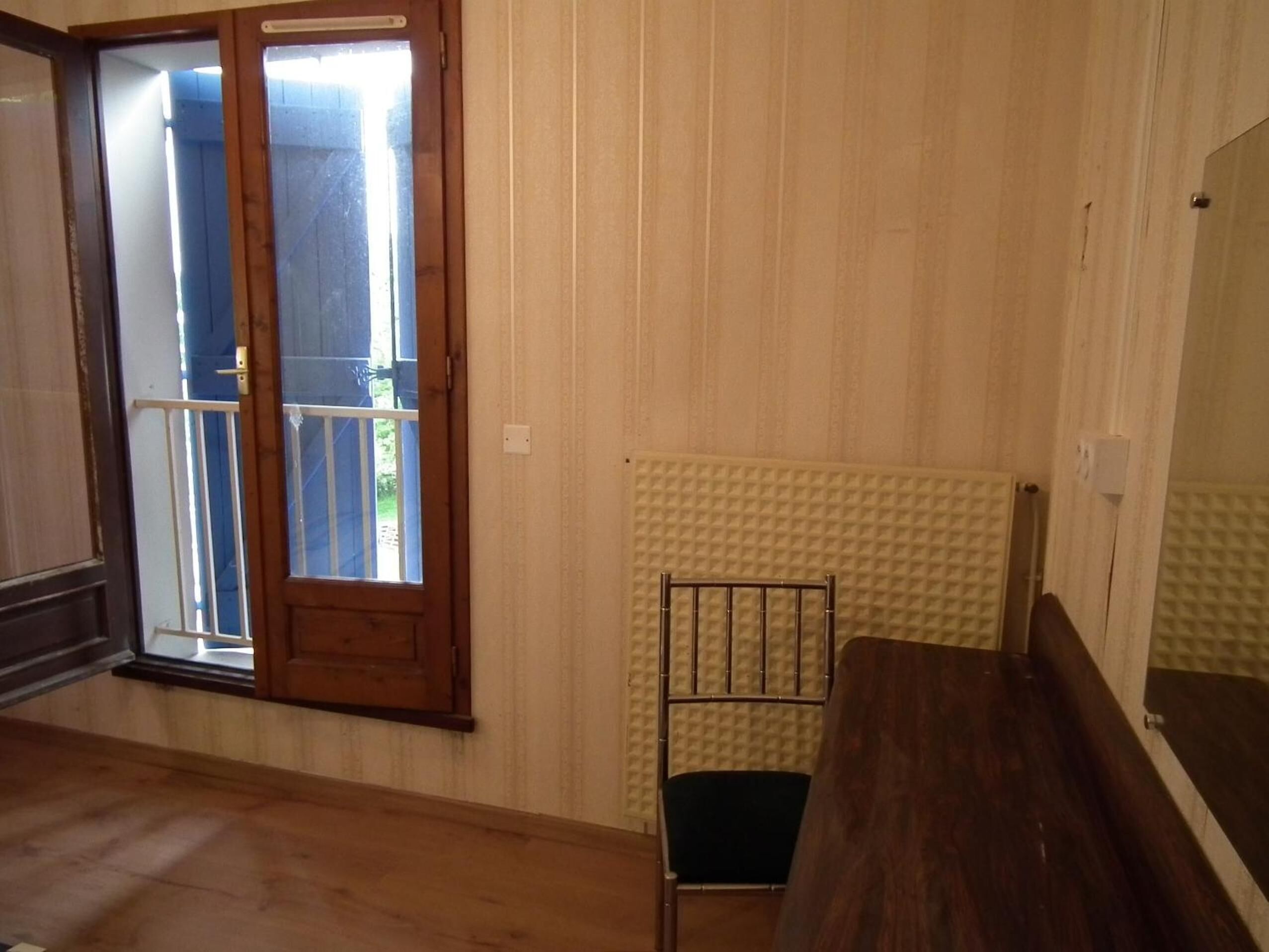 Una habitación con suelo de madera, un radiador, una silla de metal y un banco de madera.