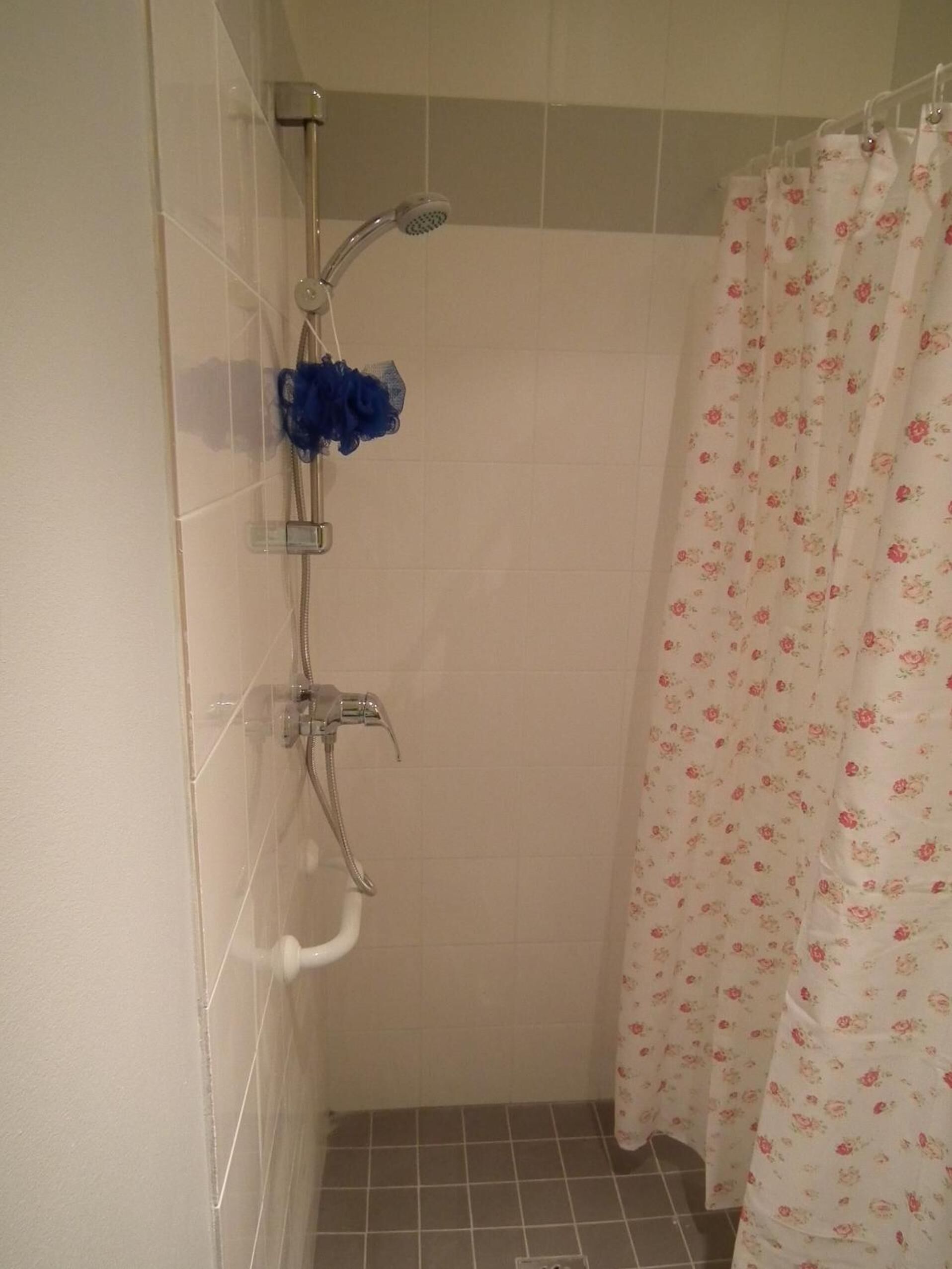 Een douche met een bloemen gordijn en een blauwe douchekop.