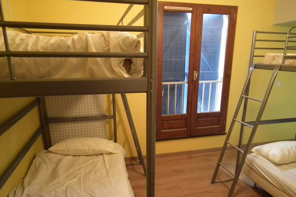 A dormitory room with bunk beds, a window with a view, and a wooden floor.