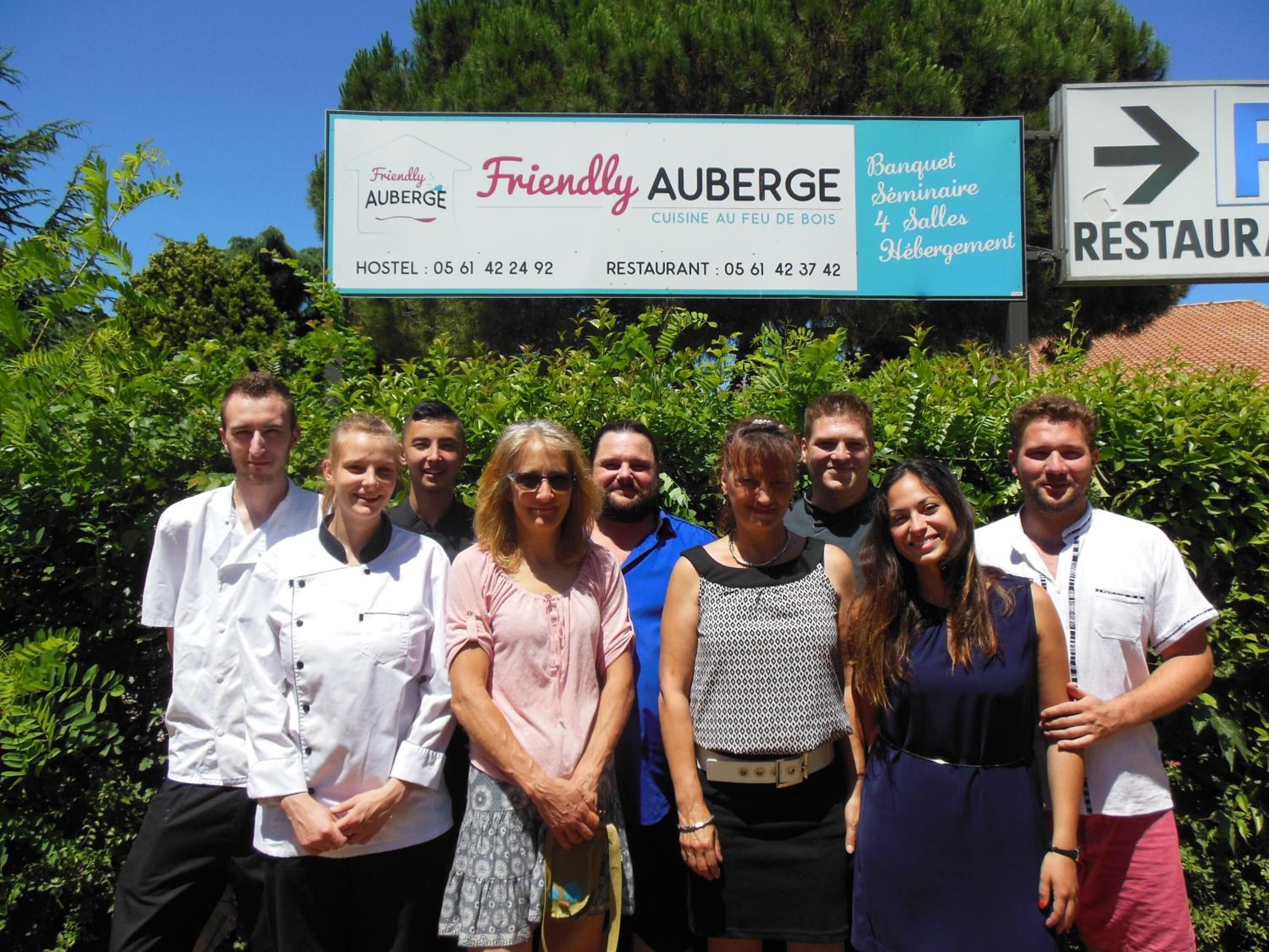 A group of people in front of a sign for Friendly Auberge, which advertises a restaurant and hostel with contact numbers.
