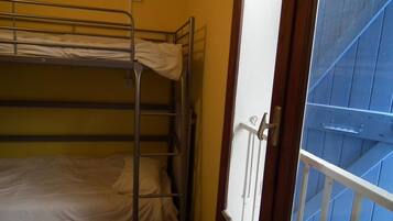 A dormitory room with bunk beds, a wooden door, and a view of a blue exterior.