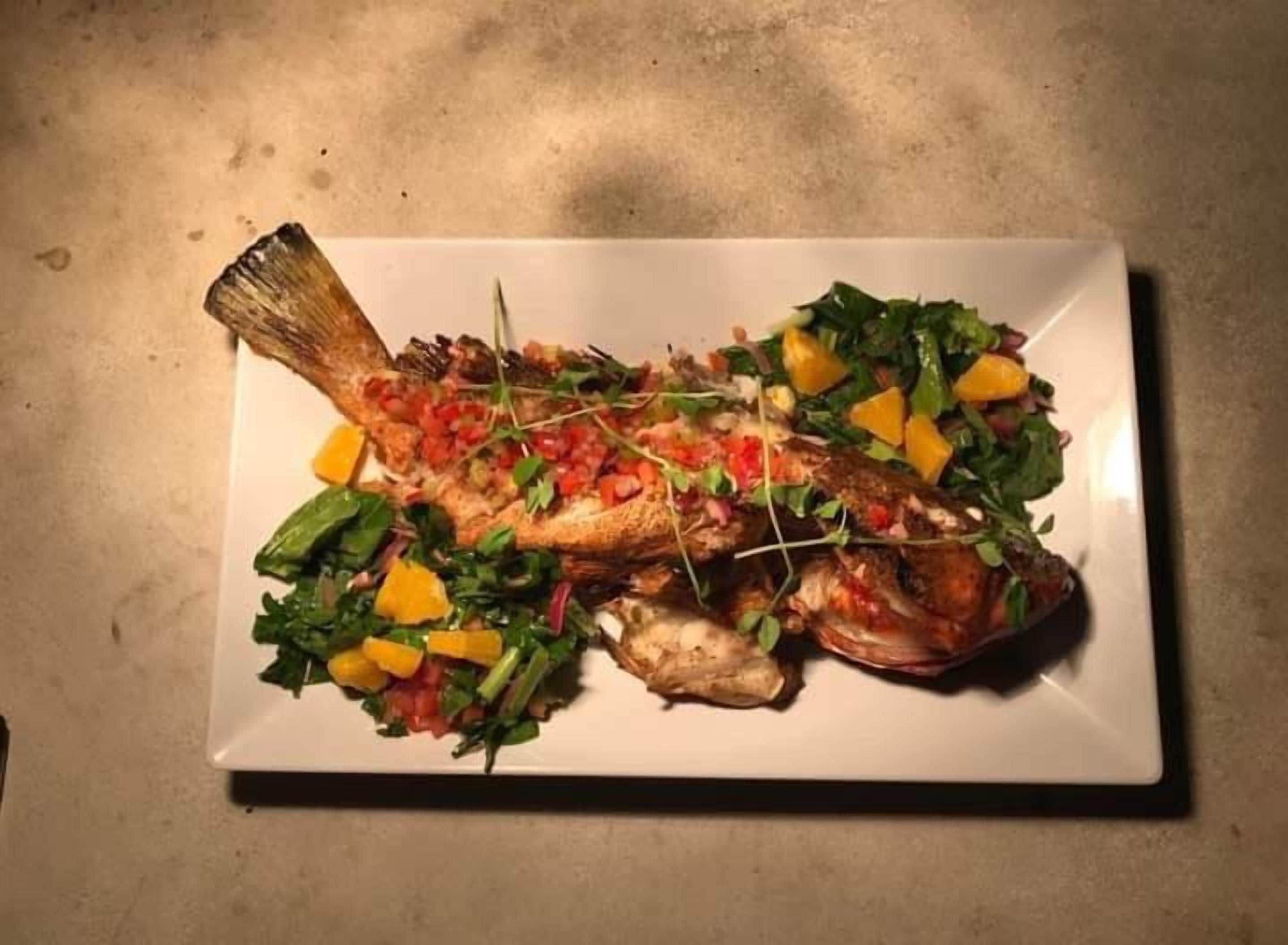 A white plate with a roasted fish garnished with vegetables and herbs.