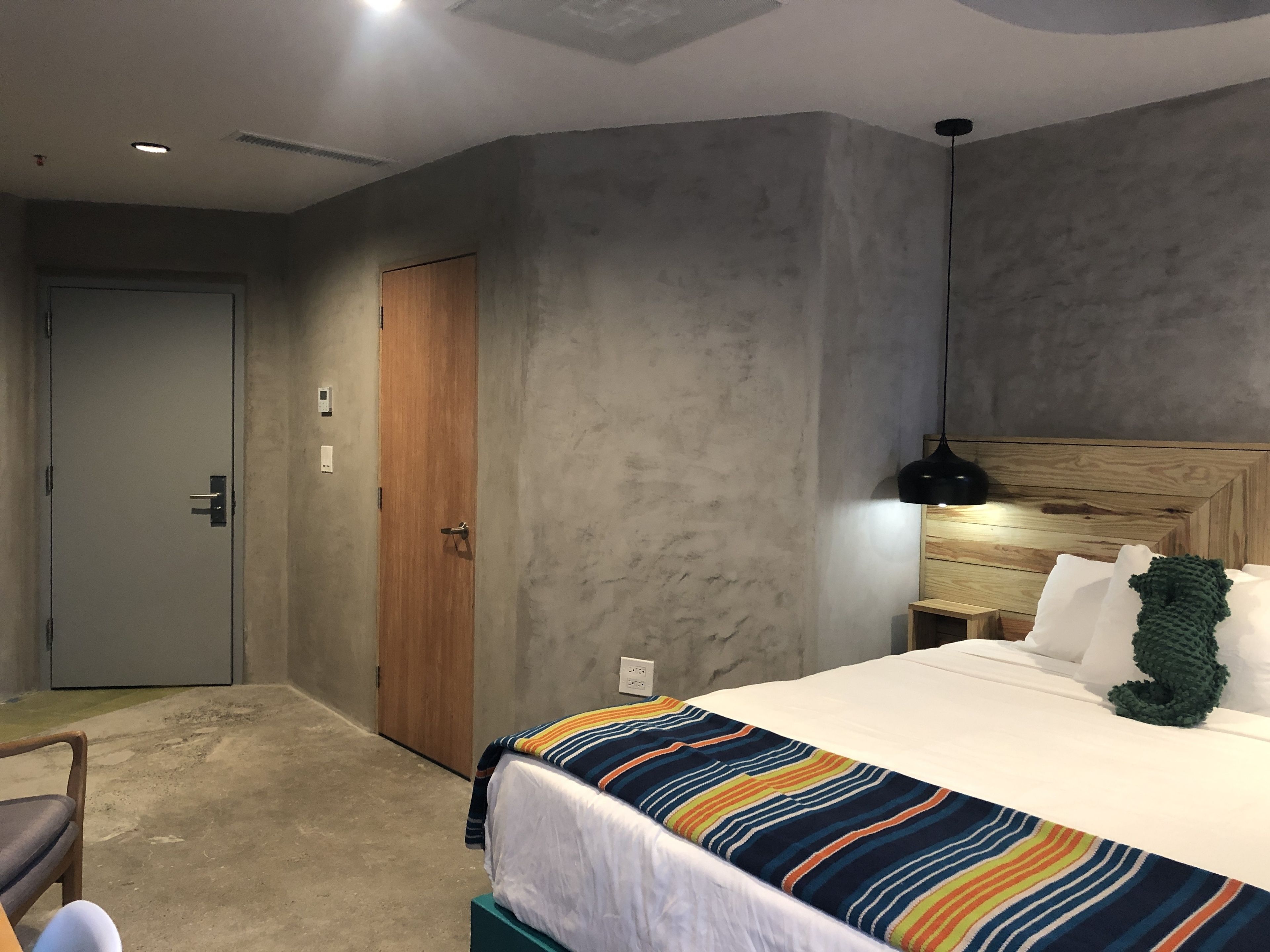 Une chambre d’hôtel avec un lit, une porte en bois, une table de chevet et une lampe fixée au mur.