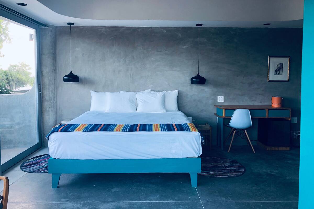 Un dormitorio moderno con una cama grande, dos lámparas colgantes, un escritorio y una silla.
