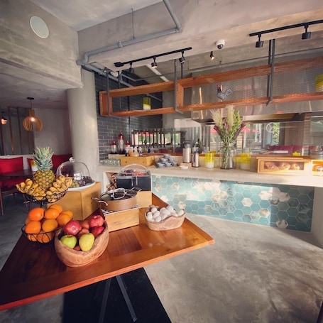 A modern kitchen with a wooden table displaying fruits and a coffee station.