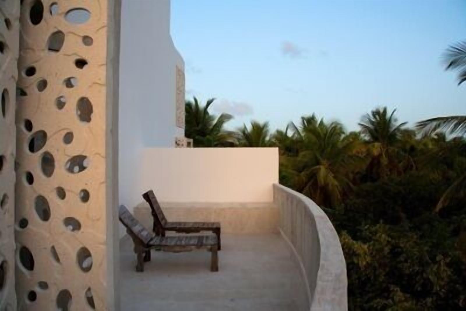 Un balcon avec un banc en bois, un mur blanc et une vue sur des palmiers.