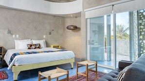 Un dormitorio moderno con cama, ventilador de techo, puerta de vidrio que da a un balcón y vistas a palmeras.