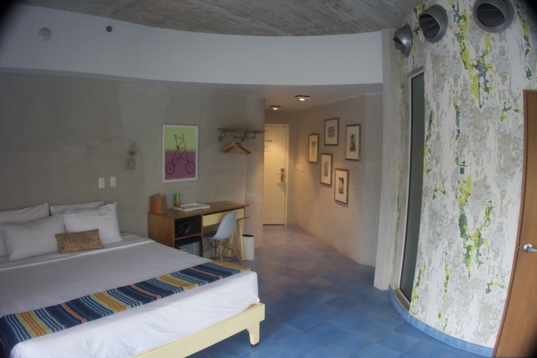 A bedroom with a bed, desk, chair, and a door leading to another room.