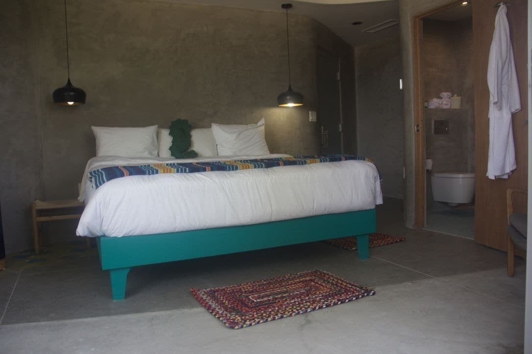 A bedroom with a teal bed, white bedding, and a patterned rug.