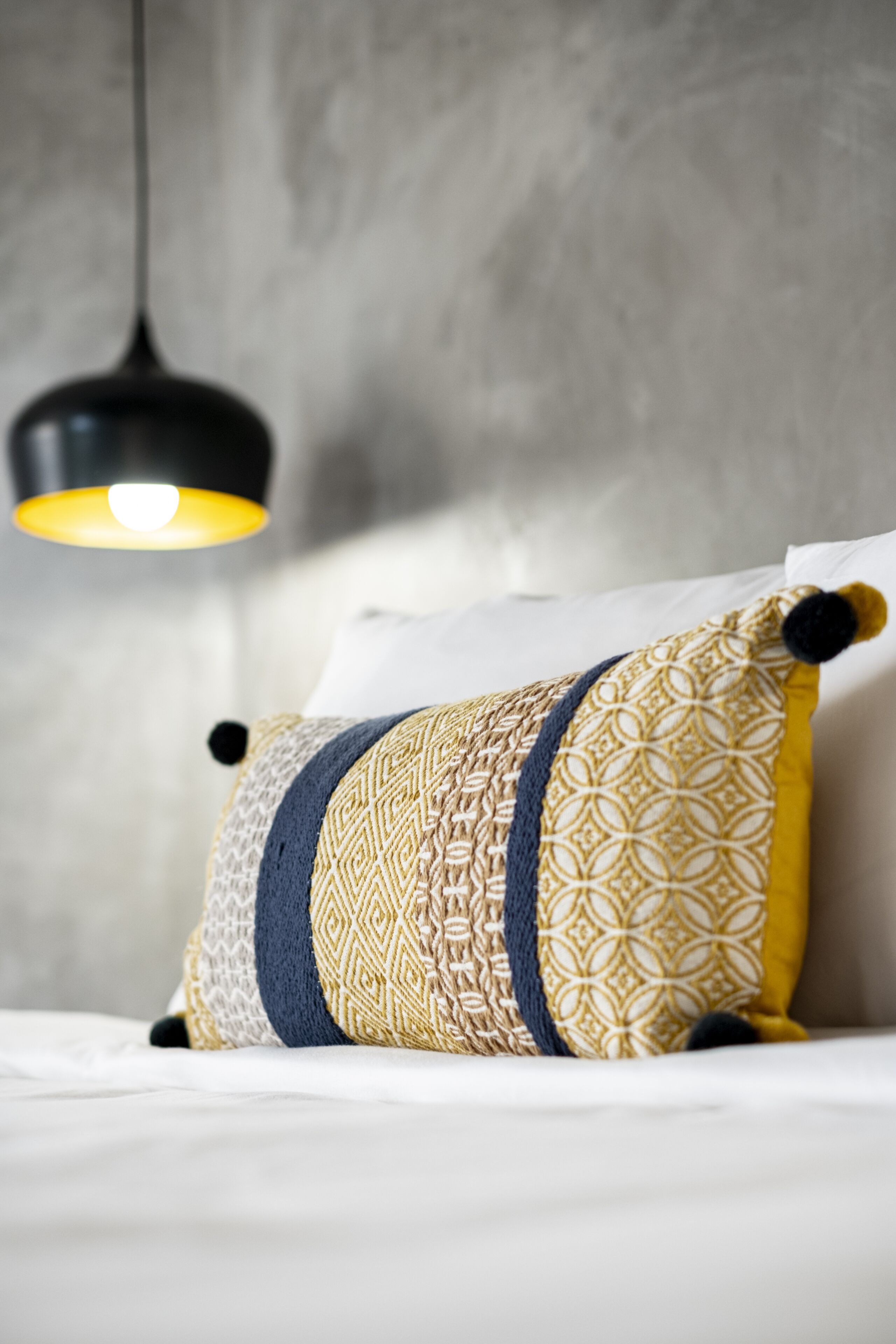 Una cama con un cojín decorativo y una lámpara colgante.
