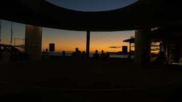A covered outdoor seating area with a view of the sunset over the water.