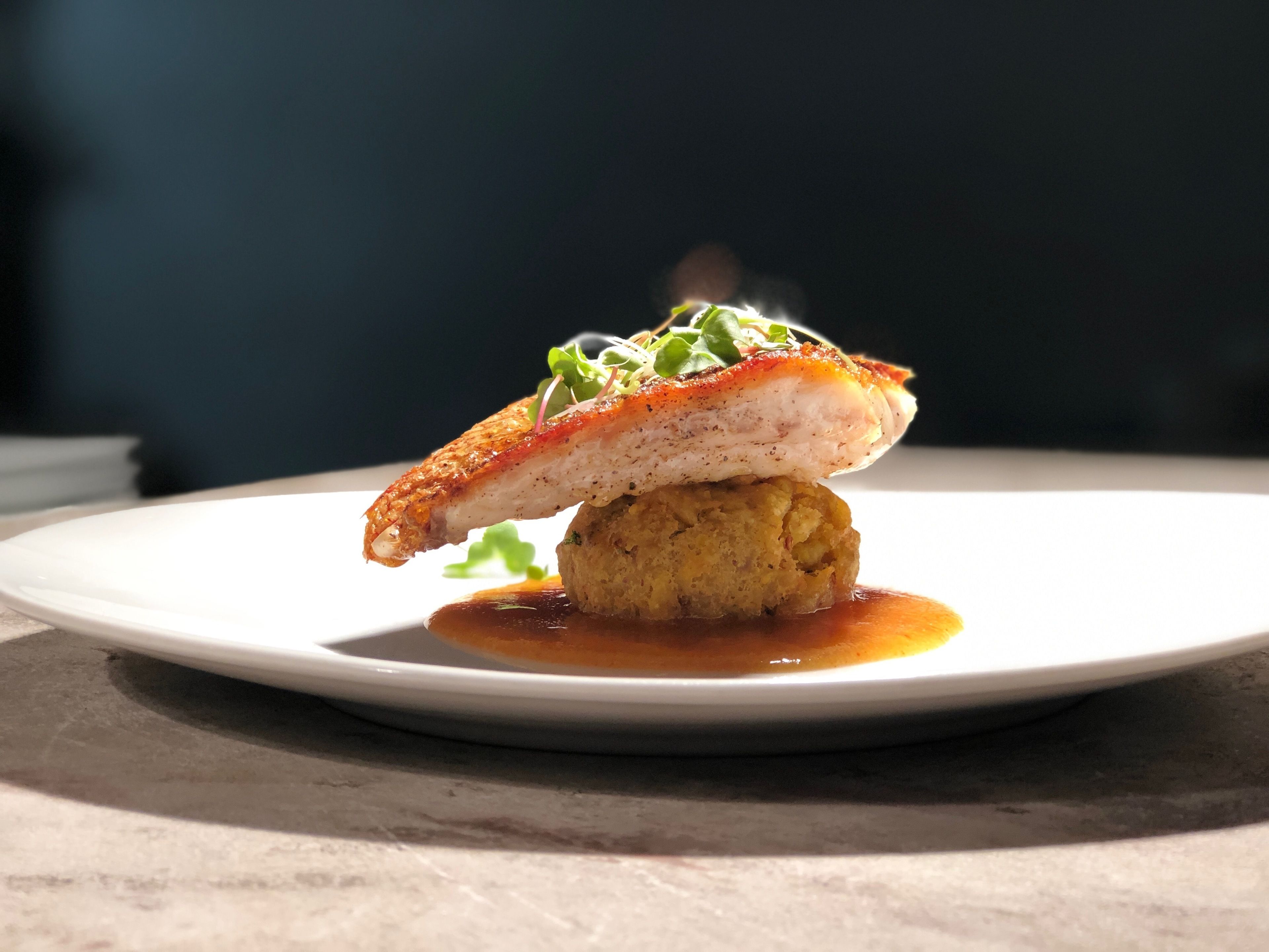 A plate with a piece of food, possibly a fish fillet, on a bed of what appears to be mashed potatoes or a similar base, accompanied by a sauce.