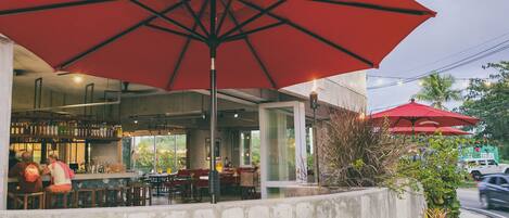 An outdoor seating area with red umbrellas, a bar, and a view of the street.