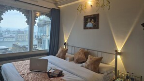 Ein Hotelzimmer mit Bett, Laptop, Büchern, einem Nachttisch mit Fernbedienung und Blick auf eine Stadtlandschaft durch ein Fenster.