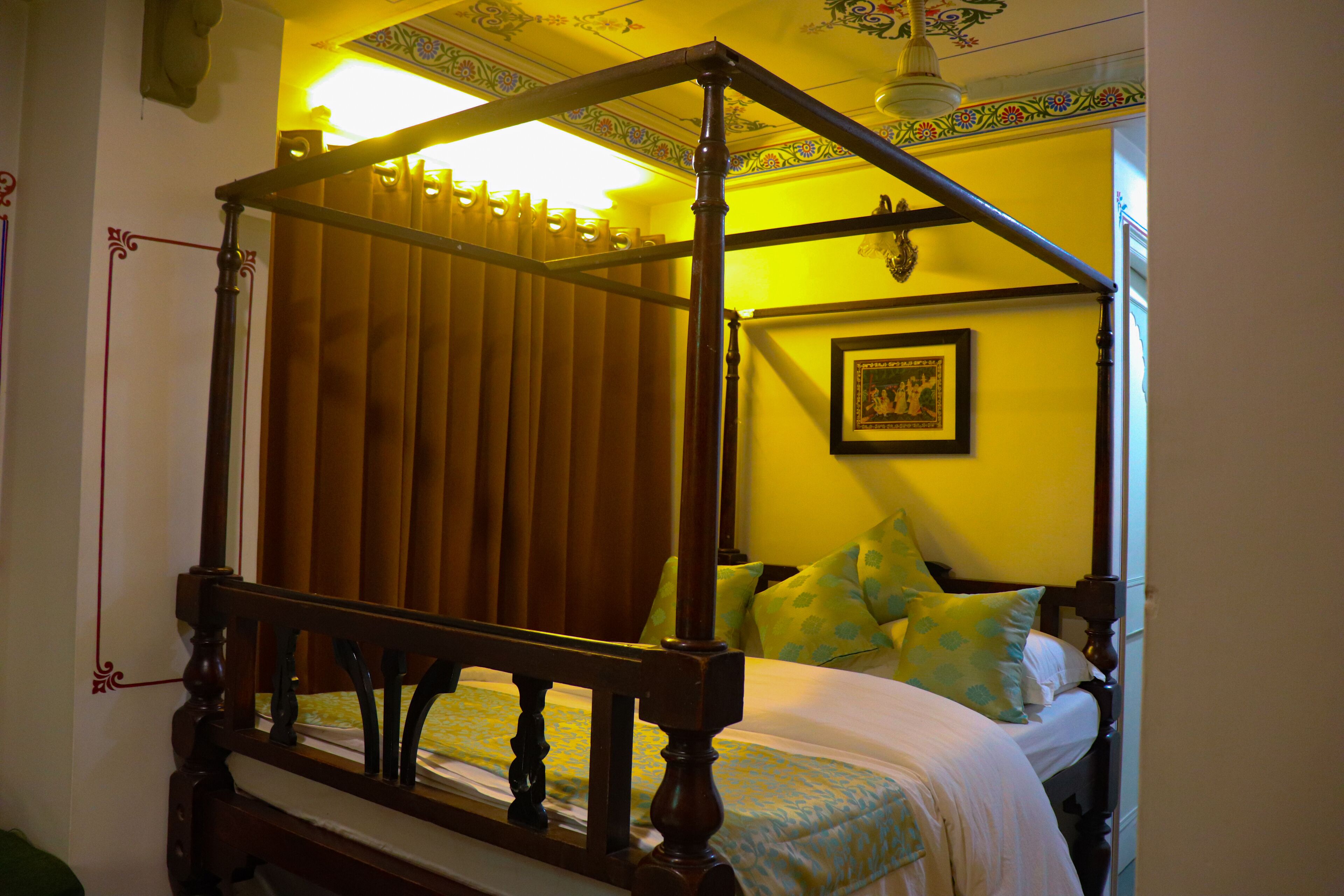Un lit à baldaquin avec un cadre en bois et un ciel de lit, un lit simple avec une couvre-lit à motifs verts et blancs, et un tableau encadré accroché au mur.