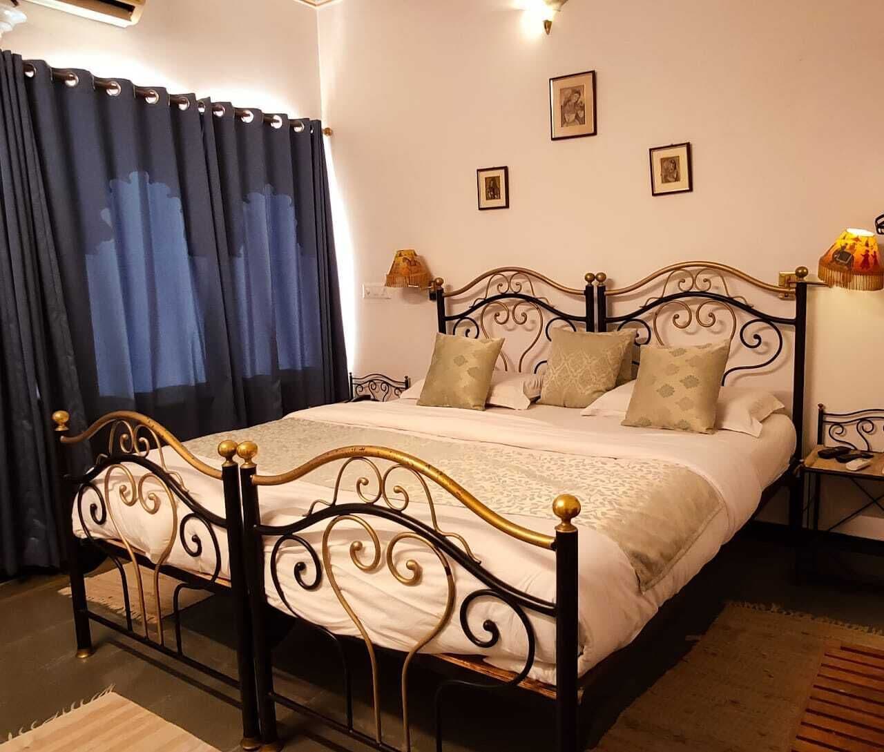 A neatly made bed with a black metal frame and gold accents, a bedside table with a lamp, and a window with blue curtains.