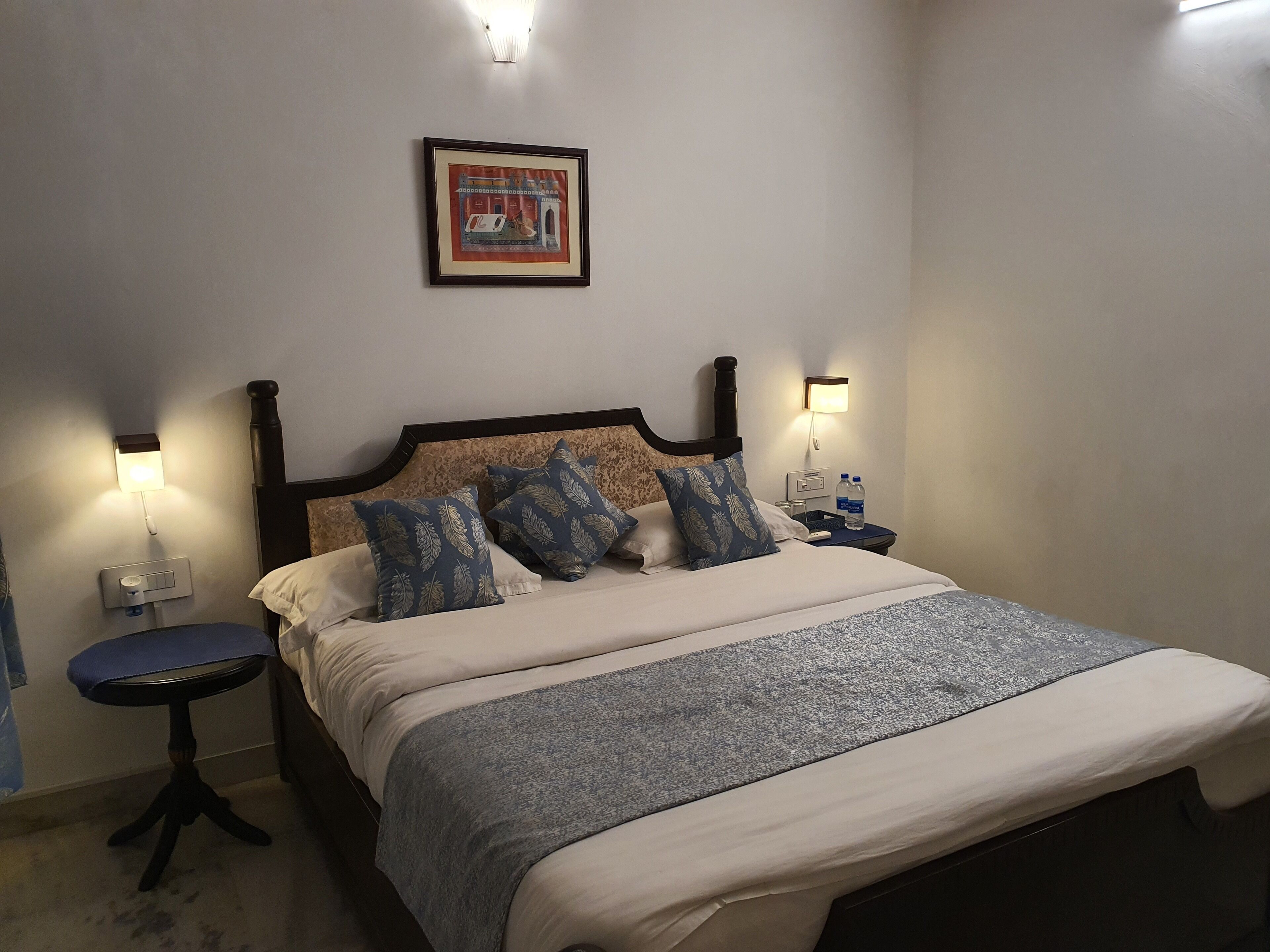 Ein ordentlich bezogenes Bett mit einer gemusterten Decke, zwei Nachttische mit Lampen und ein gerahmtes Bild an der Wand.