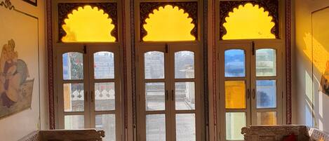 A traditional room with ornate wooden furniture, a ceiling fan, and decorative windows with intricate designs.