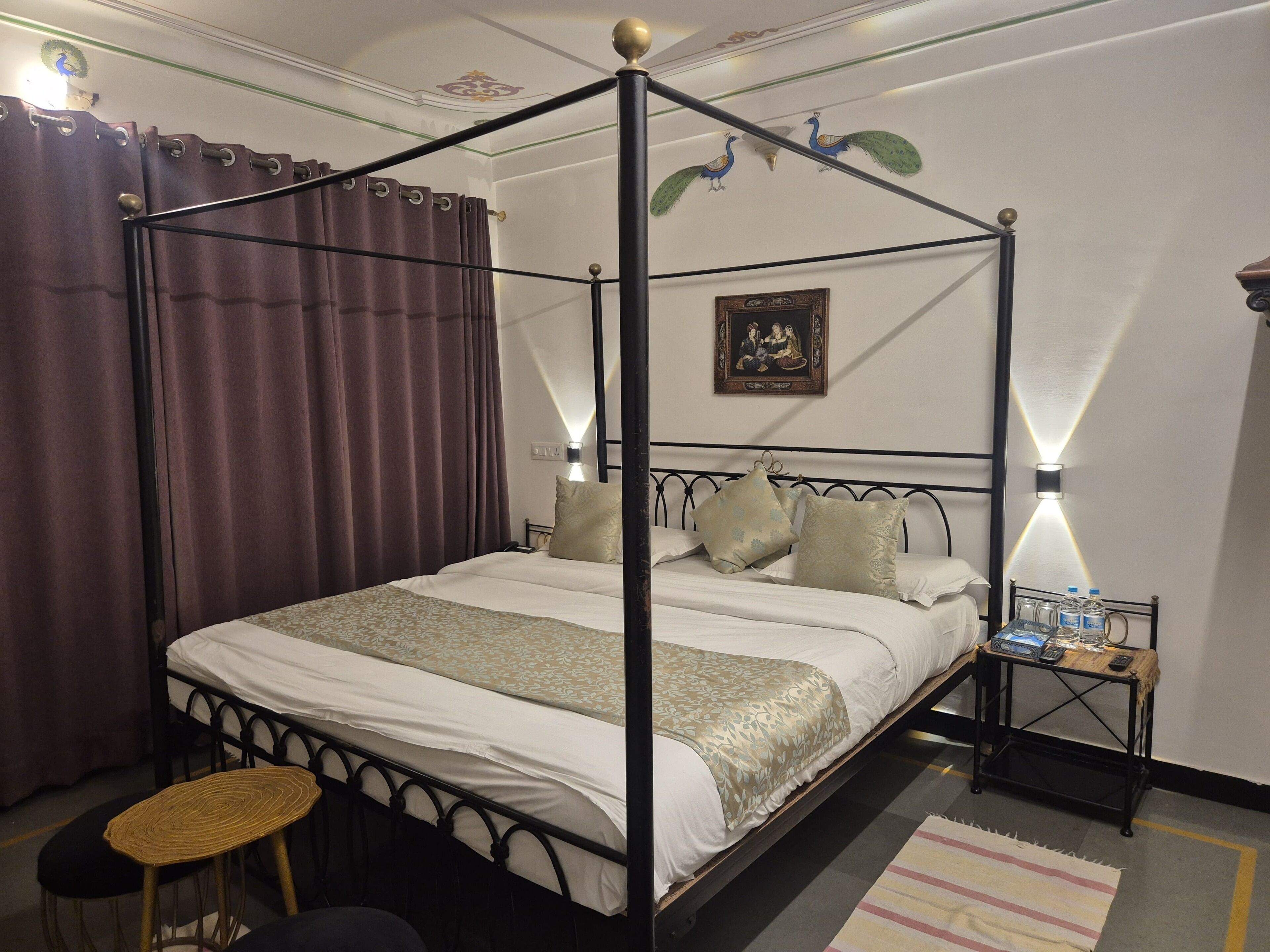 A four-poster bed with a canopy, a bedside table with a lamp, and a small stool.
