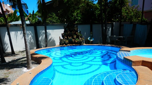 A swimming pool with a blue tiled design, surrounded by a stone deck and palm trees. - Evelyn Residence (Pattaya)