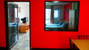 A room with a red wall, a bed, a television on a wooden stand, a table, and a mirror. - Evelyn Residence (Pattaya)