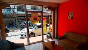 A hotel lobby with a sofa, a small table, and a large window offering a view of the street outside. - Evelyn Residence (Pattaya)