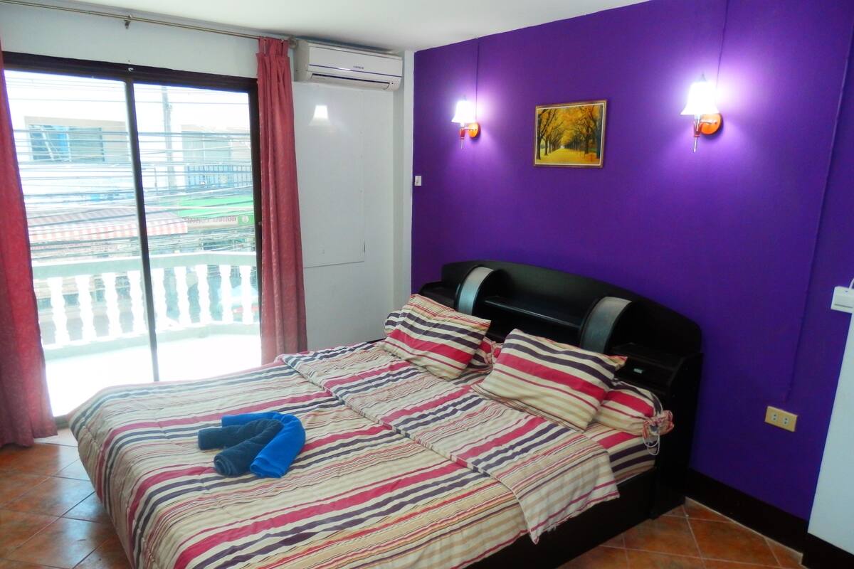 A room with a bed, purple walls, and a window with a view of buildings.