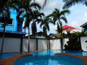 A swimming pool surrounded by palm trees and a blue building. - Evelyn Residence (Pattaya)