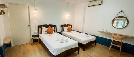 A hotel room with two single beds, a small wooden chair, a round mirror, and a shelf with a tissue box.