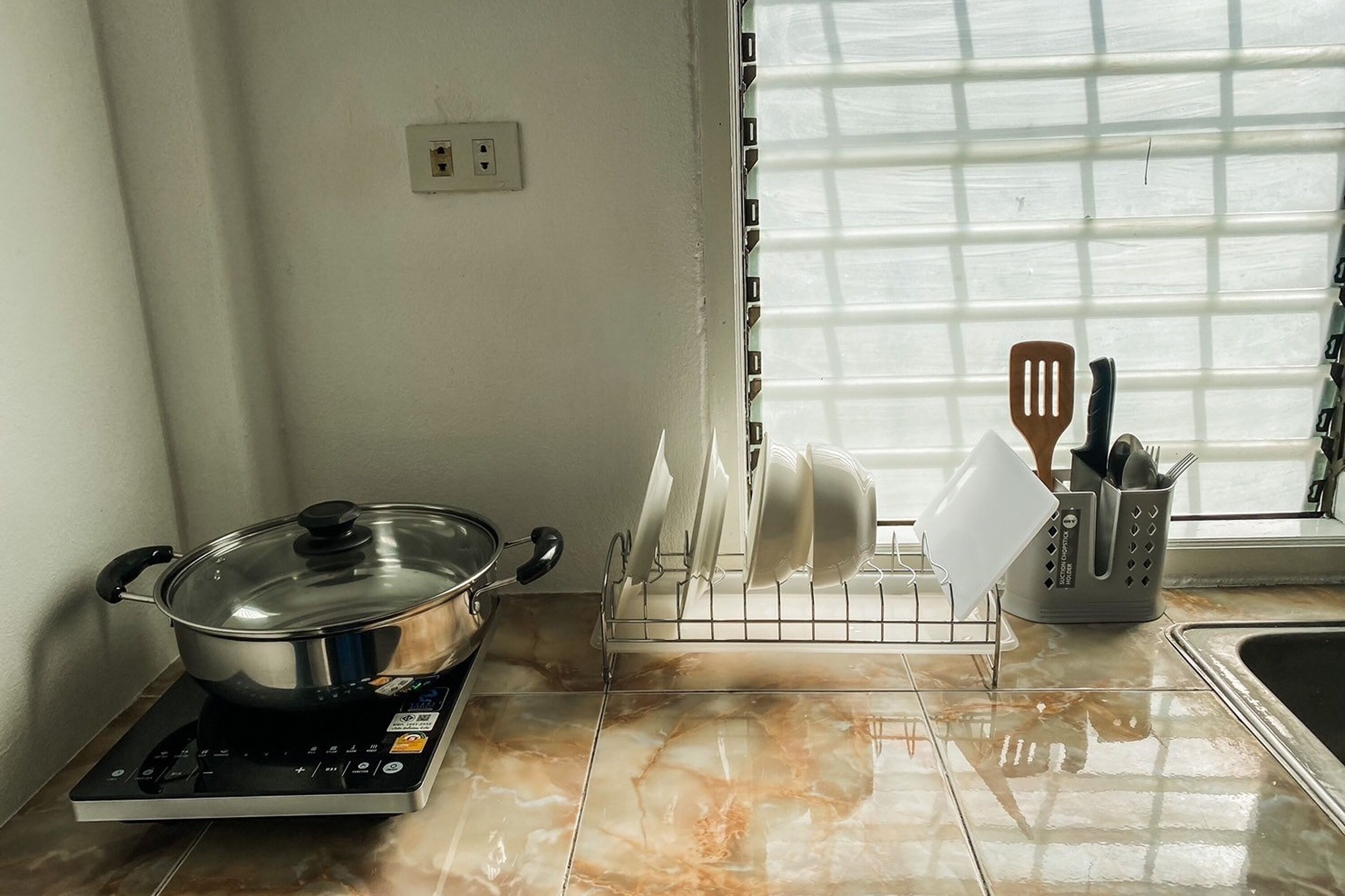 A kitchen with a stove, a dish rack, and a window with blinds.